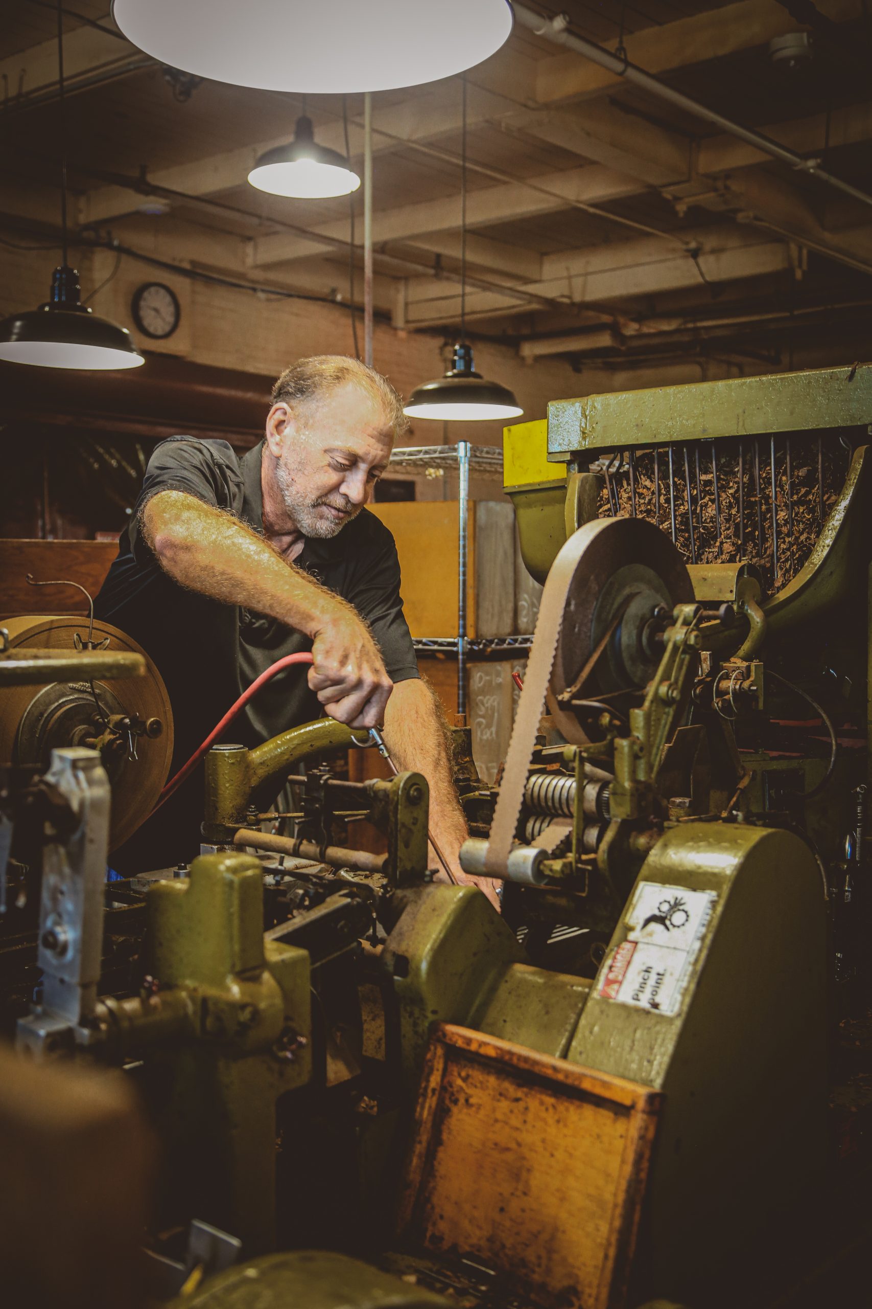 Joe St. Charles Mechnanic at J.C. Newman Cigar Co uses air gun to clean out vintage cigar rolling machines