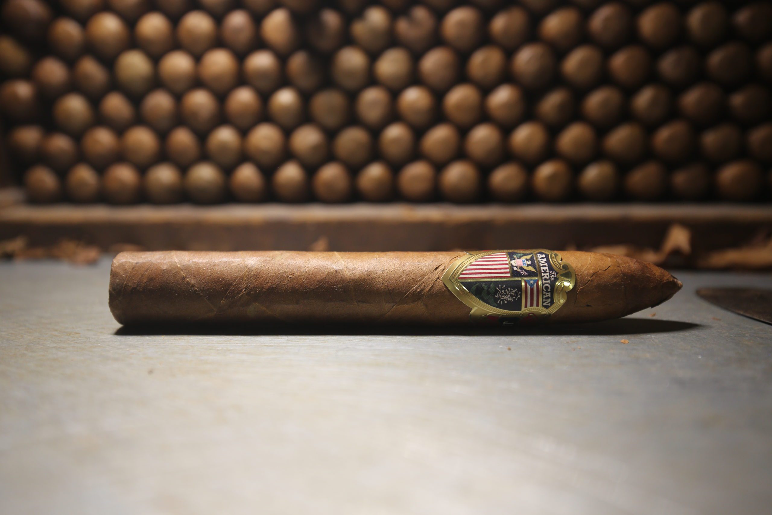 single the american torpedo cigar in front of rolled cigars in a stack