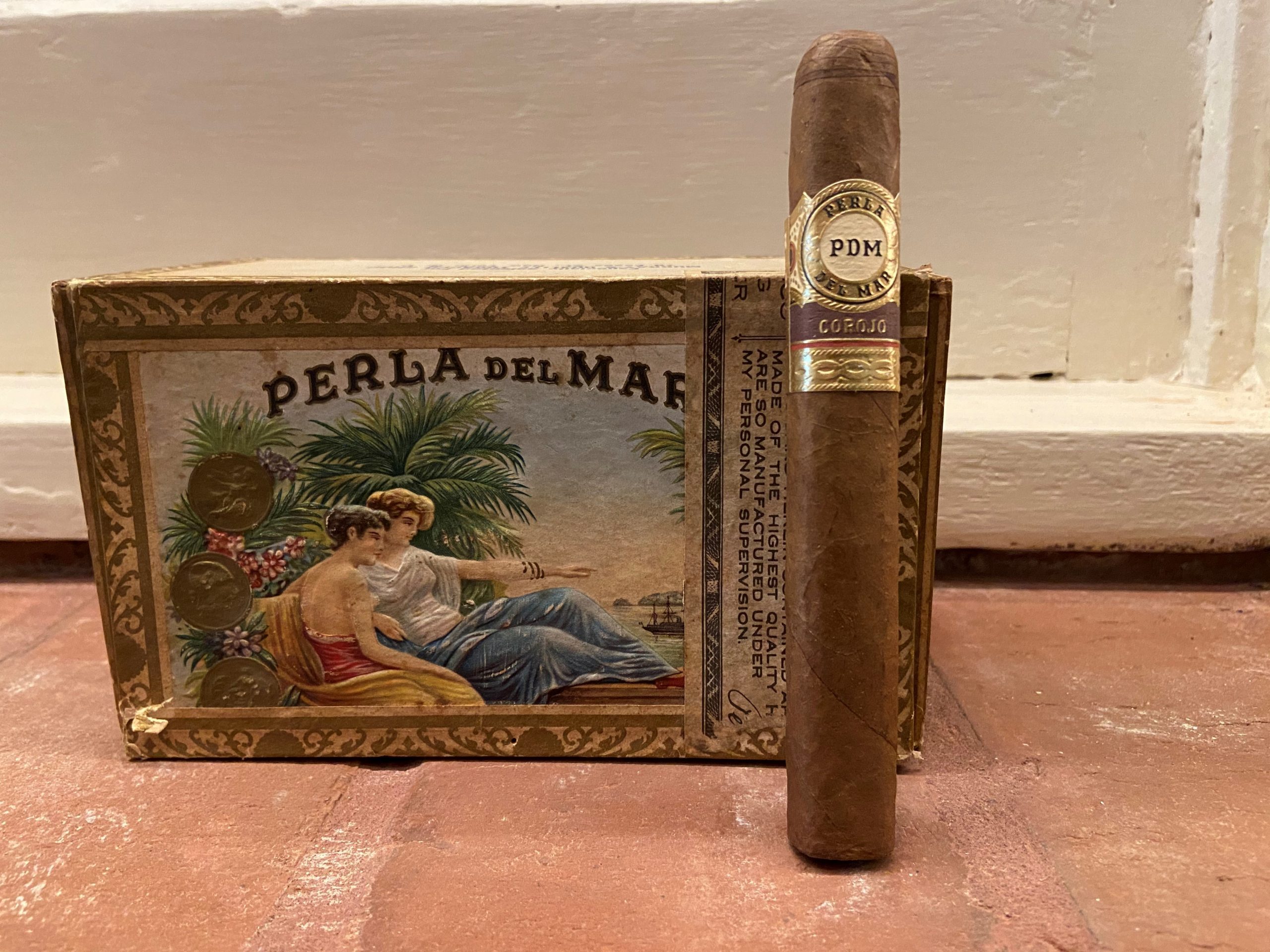 Perla Del Mar Corojo Cigar in front of a vintage Perla Del Mar Cigar Box