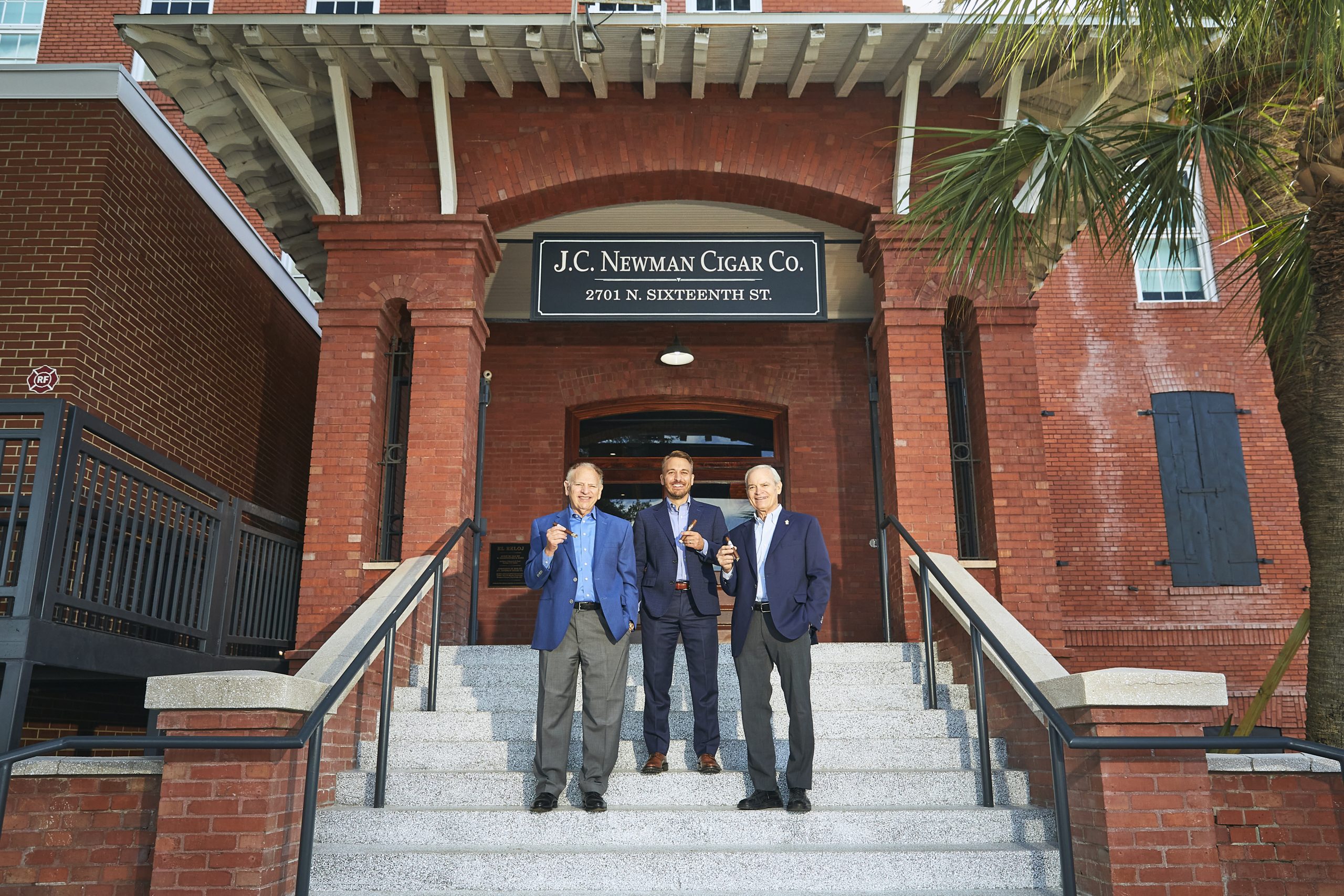 Eric Drew and Bobby Newman holding cigars on the steps of El Reloj Cigar Factory home of J.C. Newman Cigar Co.